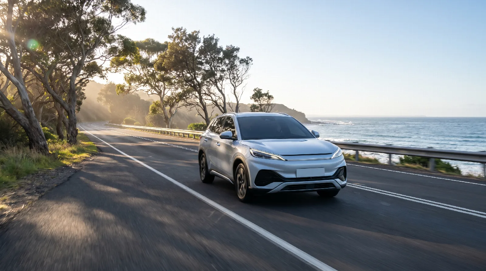 A compact electric SUV driving along an Australian coastal road beside gum trees and the ocean